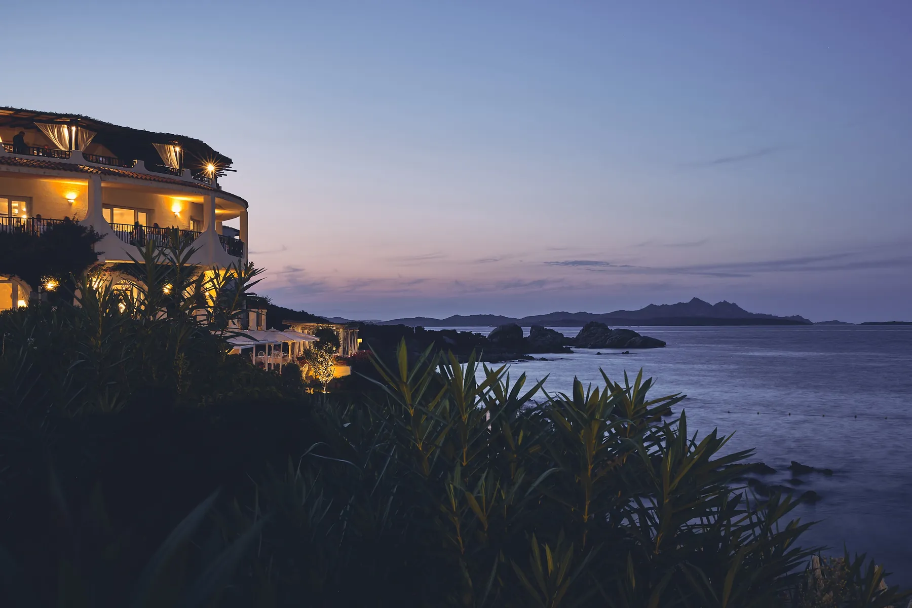 Resort lit at dusk above the sea, with islands on the horizon